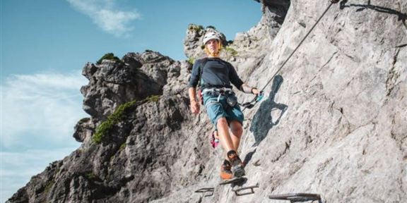 Ein Kletterer helmet an einer felsigen Wand. Er benutzt Sicherungsanlagen, um sich sicher nach oben zu bewegen.