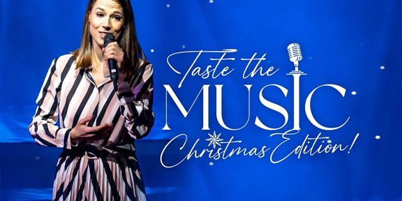 Eine Frau steht auf der Bühne und singt in ein Mikrofon. Im Hintergrund ist eine festliche Weihnachtsdekoration zu sehen.