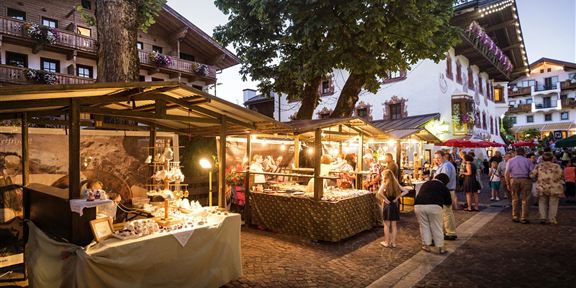 A lively marketplace at twilight with stalls offering local products. People stroll through the alleys and enjoy the atmosphere.