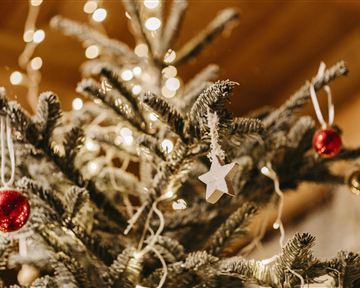 Ein festlich geschmückter Weihnachtsbaum steht im Schnee vor einer beleuchteten Kirche. Die Szenerie ist nachts und strahlt eine gemütliche Stimmung aus.