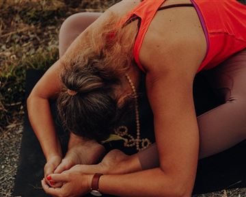 A person is doing a yoga pose on a mat outdoors. They are bending forward and holding a foot.