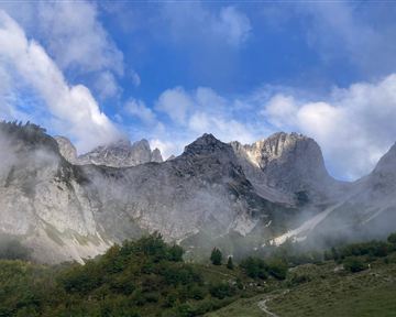 An impressive mountain panorama with rocky peaks and light wisps offog. The sky is clear with a few clouds.