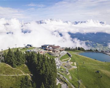 A beautiful mountain landscape with fog and a clear lake. In the background, a restaurant and hiking trails can be seen.