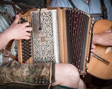 A musician plays an accordion while another musician holds a guitar. Both are wearing traditional clothing.