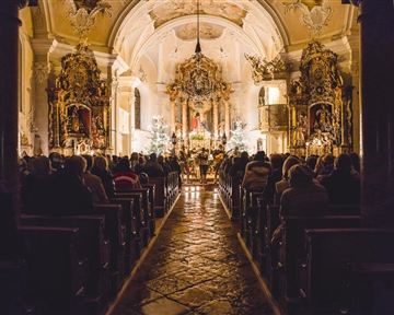 An atmospheric church with many people sitting in the dark. The space is festively decorated and warmly lit.