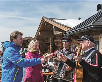 Eine Gruppe von Freunden stößt mit Biergläsern an. Sie sitzen an einem Tisch und genießen die gemeinsame Zeit in einer gemütlichen Umgebung.