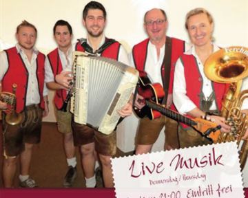 A group of four musicians in traditional costumes stands on stage. They play different instruments and promote a live music event at the Hexenalm hotel.