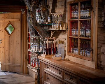 Ein gemütlicher Raum mit einer Holzküche und Regalen, die mit Flaschen gefüllt sind. Eine offene Tür mit grünem Fensterdetail lädt zum Eintreten ein.