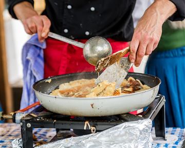 A person is cooking in a pan on a gas stove. You can see them flipping the food with a spatula.
