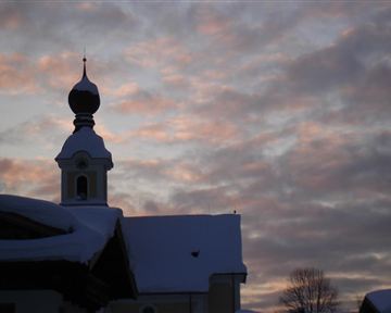 Eine sanfte Silhouette eines Gebäudes mit einem kuppelähnlichen Turm, umgeben von Schnee. Der Himmel zeigt ein Farbenspiel aus Rosa und Grau in der Dämmerung.