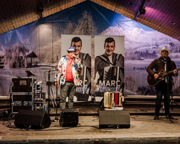 A live performance by two musicians on a stage. In the background, there are large posters of Marc Pichler visible.