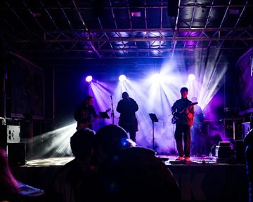 Three musicians are sitting on chairs. One is playing the accordion, one is playing the violin, and the third is playing a flute.