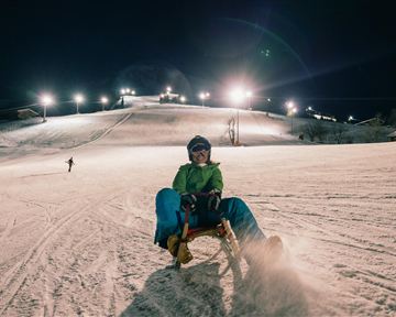 Eine nächtliche Skisession auf einer beleuchteten Piste. Skifahrer fahren den Hang hinunter, während die Lichter die Landschaft erhellen.