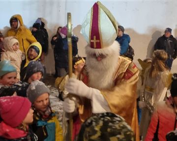 Ein festlicher Anlass mit vielen Kindern, die um eine historische Figur versammelt sind. Der Mann in dem goldenen Gewand hat einen langen Bart und trägt eine Mitra.