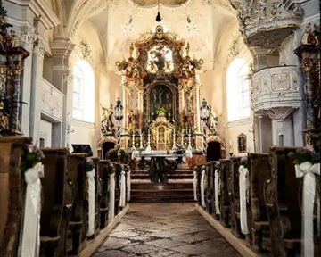 Eine prächtige Kirche mit einer kunstvoll gestalteten Innenausstattung. Der Blick führt den langen Weg zum Altar, umgeben von eleganten Sitzbänken.