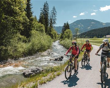 Ein natürlicher Felsen mit einer Öffnung, die einen Blick auf einen ruhigen See und Hügel gewähren. Der Himmel ist klar und blau.