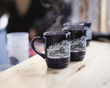 Dampfen Sie Tassen auf einem Holztisch. Die Tassen sind schwarz und haben ein dekoratives Muster.