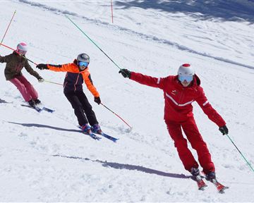 Drei Skifahrer fahren die Piste hinunter. Sie tragen helle Skikleidung und genießen den Schnee.