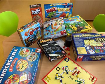 Eine Auswahl von Brettspielen liegt auf einem Tisch. Die Spiele sind bunt und reichen von klassischen bis zu modernen Kinderspielen.