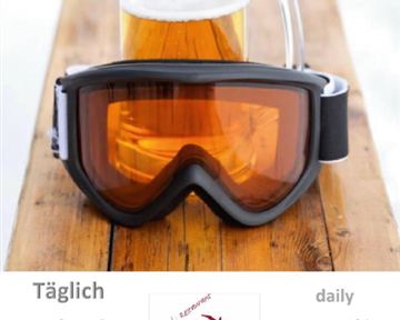 Ein Bierglas steht auf einem Holztisch neben einer Skibrille. Darüber steht die Ankündigung einer täglichen Après-Ski-Party mit DJ.