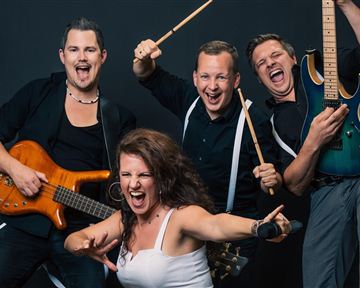 Eine lebendige Band mit vier Mitgliedern posiert enthusiastisch für das Foto. Sie halten Musikinstrumente und zeigen Freude und Energie auf der Bühne.