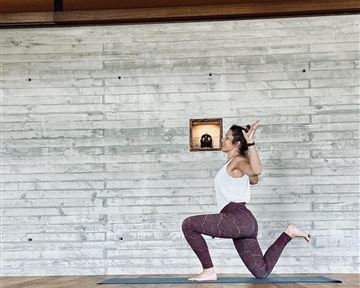 Eine Person übt Yoga in einer modernen Umgebung mit Holz- und Betonwänden. Sie zeigt eine dehnbare Pose auf einer Matte.