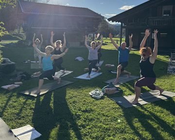A group of people is doing yoga outdoors under a clear sky. The sun is shining, and the atmosphere is relaxed.