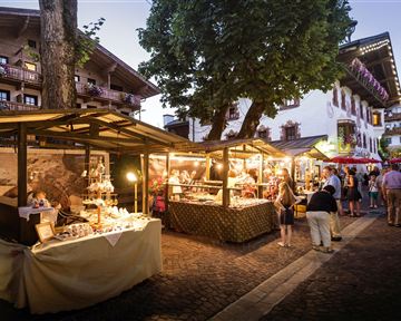 A lively marketplace at twilight with stalls offering local products. People stroll through the alleys and enjoy the atmosphere.