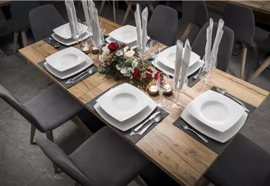 Ein elegant gedeckter Tisch aus Holz mit weißem Geschirr und Dekoration in Form von Blumen. Die Atmosphäre ist gemütlich und einladend.