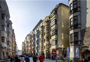 A bustling street with colorful buildings and pedestrians. Cafés and bicycles can be seen in the background.