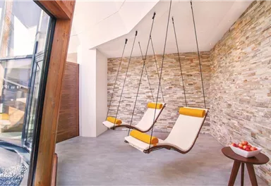 Ein moderner Raum mit zwei hängenden Liegestühlen und einer attraktiven Steinwand. Neben den Stühlen steht ein kleiner Tisch mit Äpfeln.