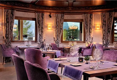 An elegant restaurant with purple furniture and beautiful table decorations. Large windows provide a view of the nature outside.