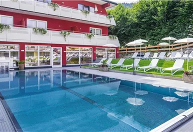 Ein schöner Pool mit Liegen und Sonnenschirmen im Freien. Im Hintergrund ist ein modernes Gebäude mit Balkonen sichtbar.