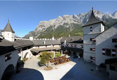A picturesque courtyard of a castle with impressive mountains in the background. The surroundings are calm and inviting, ideal for visitors.
