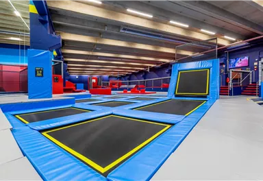 Eine moderne Trampolinhalle mit mehreren Trampolinen und farbenfrohen Wänden. Die Atmosphäre ist einladend und ideal für sportliche Aktivitäten.