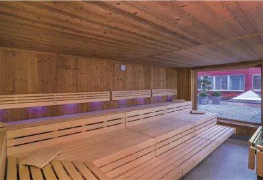 Eine moderne Sauna mit Holzoberflächen und bequemen Liegen. Durch die großen Fenster blickt man in einen gemütlichen Außenbereich.