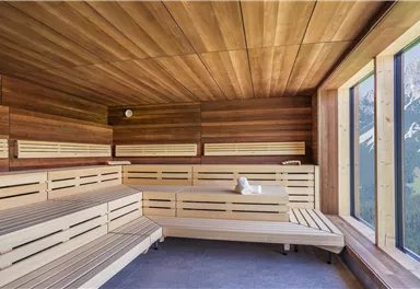 Ein modernes Saunainterior mit Holzverkleidung und großen Fenstern. Der Blick fällt auf eine beeindruckende Berglandschaft.