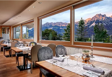 An elegant restaurant with wooden tables and stylish chairs. The large windows offer a view of majestic mountains and a beautiful landscape.