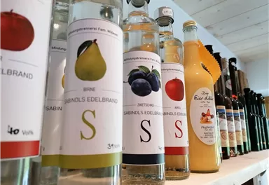 Shelf with bottles of various fruit brandies and juices. The labels show fruits such as pear, plum, and apple.