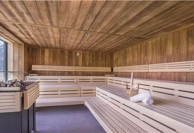 Eine moderne Sauna mit Holzverkleidung und Bänken aus hellem Holz. Durch große Fenster kann man die Aussicht auf die Natur genießen.