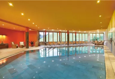 Ein modernes Hallenbad mit glattem Wasser und bequemen Liegen. Große Fenster bieten einen Blick auf die grüne Umgebung.