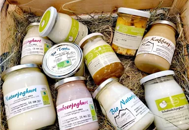 A selection of yogurt and dairy products in a wooden basket. The jars are labeled and vary in flavor and type.