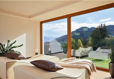 A cozy room with two loungers and large windows. In the background, you can see a picturesque mountain landscape under a clear sky.