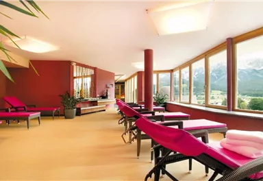 Ein heller Entspannungsraum mit pinken Liegestühlen und großen Fenstern. Der Blick bietet eine schöne Aussicht auf die Berge.