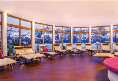 A bright relaxation room with comfortable loungers and large windows. In the background, snow-covered mountains and a beautiful sunset can be seen.