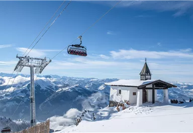 Eine schneebedeckte Berglandschaft mit einer Seilbahn und einem kleinen Gebäude. Der Himmel ist klar und blau, mit beeindruckenden Bergen im Hintergrund.