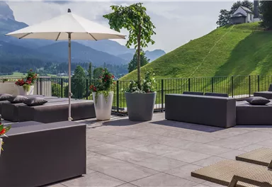 Eine moderne Terrasse mit bequemen Sitzmöbeln und Sonnenschirmen. Im Hintergrund erstreckt sich eine grüne Landschaft mit sanften Hügeln.
