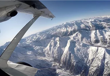 Eine atemberaubende Berglandschaft mit schneebedeckten Gipfeln und klarem blauem Himmel. Im Vordergrund ist das Flugzeug mit einem Propeller zu sehen.