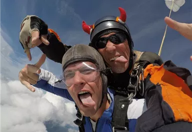 Zwei Fallschirmspringer machen Selfies im freien Fall. Beide zeigen ihre Zunge und haben Spaß in der Luft.