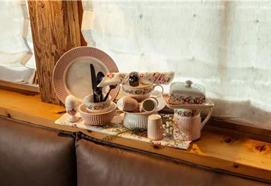 A rustic table with various tea set elements. The pieces are decorated in soft colors with floral motifs.